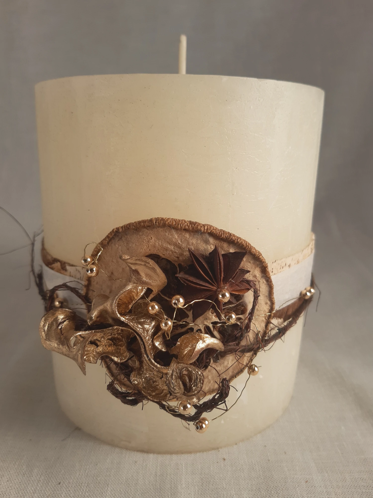 Jolie bougie couleur crème de 20 cm de diamètre, décorée pour Noël par une ceinture d'éléments naturels. Ecorce d'eucalyptus, perles, ruban, fil de fer, cosses, étoiles d'anis et autre.